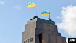 Украинские флаги развеваются на месте памятника Ленину, который был сброшен протестующими накануне вечером в Харькове 29 сентября 2014 года. Украинцы, протестующие в Харькове, сбросили гигантскую статую, которая считалась символом советского наследия